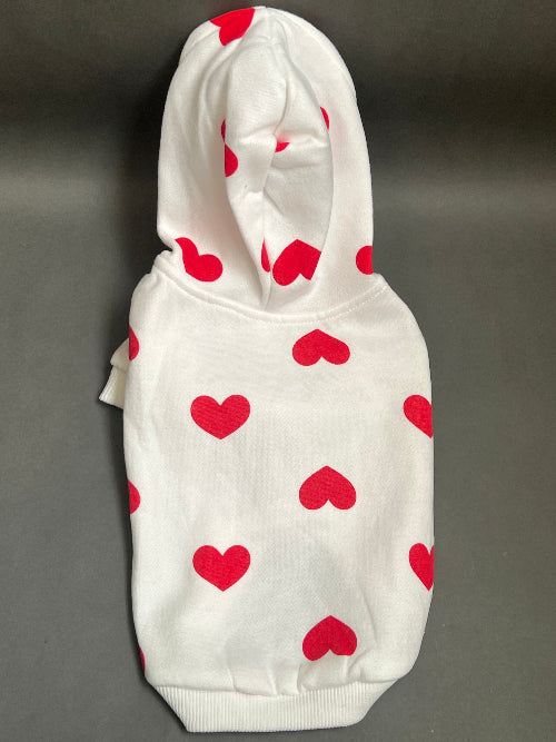 UNA SUDADERA CON CAPUCHA EN COLOR BLANCO Y ESTAMPADO DE CORAZONES ROJO. MANGA LARGA, SE METE TIPO JERSEY, SIN CIERRES NI BOTONES. ES CALIENTITA PORQUE POR DENTRO ES UNA FELPITA DE PIEL DE DURAZNO.