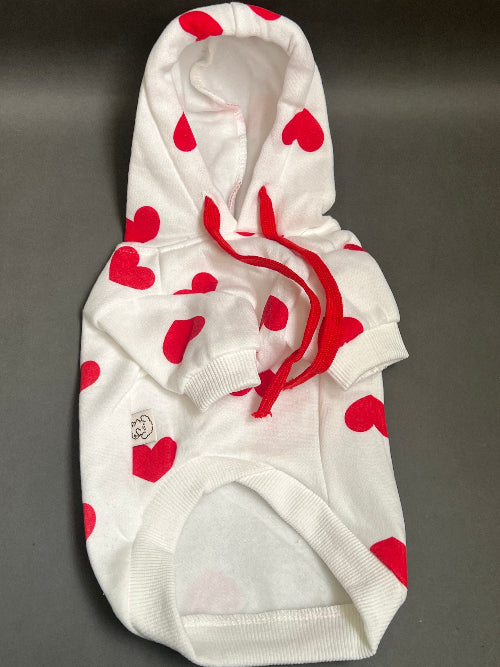 UNA SUDADERA CON CAPUCHA EN COLOR BLANCO Y ESTAMPADO DE CORAZONES ROJO. MANGA LARGA, SE METE TIPO JERSEY, SIN CIERRES NI BOTONES. ES CALIENTITA PORQUE POR DENTRO ES UNA FELPITA DE PIEL DE DURAZNO.