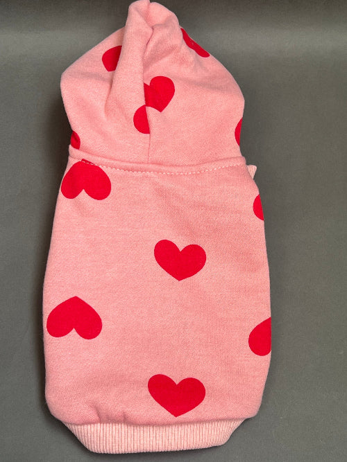 UNA SUDADERA CON CAPUCHA EN COLOR ROSA Y ESTAMPADO DE CORAZONES ROJO. MANGA LARGA, SE METE TIPO JERSEY, SIN CIERRES NI BOTONES. ES CALIENTITA PORQUE POR DENTRO ES UNA FELPITA DE PIEL DE DURAZNO.