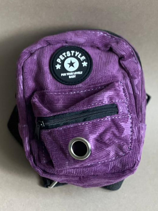 mochila morada para perro de varios colores para que cargue sus premios y bolsitas. Es liviana por lo que no le pesa.