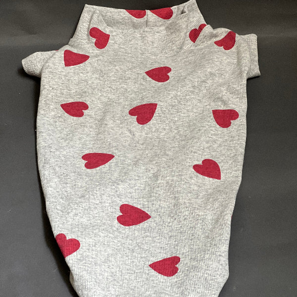 SUÉTER DE TELA ACANALADA Y ESTAMPADO DE CORAZONES, CUELLO ALTO PERO NO ES GRUESO. VISTE Y ES COMODO ES SUETER POR LO QUE NO TIENE BOTONES O CIERRE. COLOR GRIS ESTAMPADO CORZONES ROJOS.