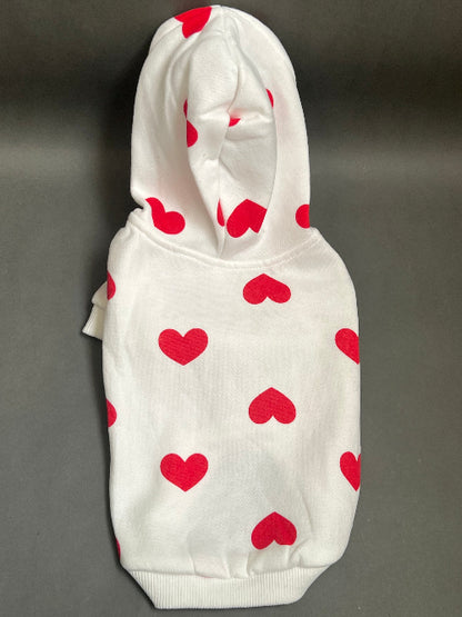 UNA SUDADERA CON CAPUCHA EN COLOR BLANCO Y ESTAMPADO DE CORAZONES ROJO. MANGA LARGA, SE METE TIPO JERSEY, SIN CIERRES NI BOTONES. ES CALIENTITA PORQUE POR DENTRO ES UNA FELPITA DE PIEL DE DURAZNO.
