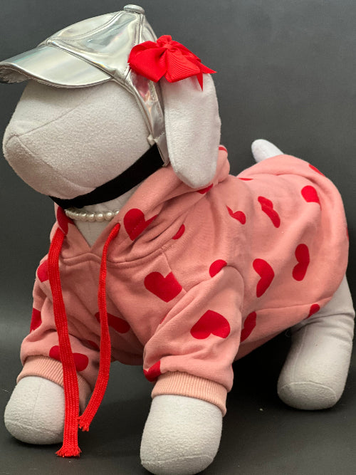 UNA SUDADERA CON CAPUCHA EN COLOR ROSA Y ESTAMPADO DE CORAZONES ROJO. MANGA LARGA, SE METE TIPO JERSEY, SIN CIERRES NI BOTONES. ES CALIENTITA PORQUE POR DENTRO ES UNA FELPITA DE PIEL DE DURAZNO.