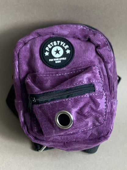 mochila morada para perro de varios colores para que cargue sus premios y bolsitas. Es liviana por lo que no le pesa.